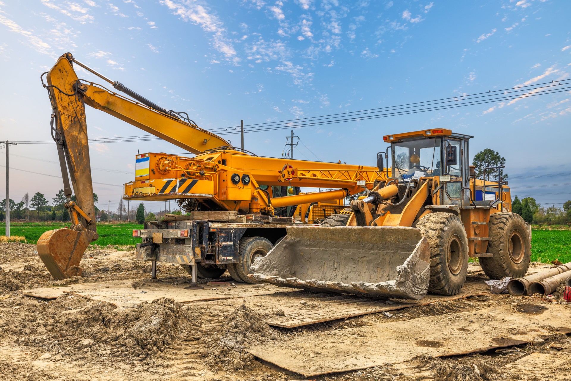 Yellow wheel loader and excavator machinery parked on muddy ground at outdoor construction site.