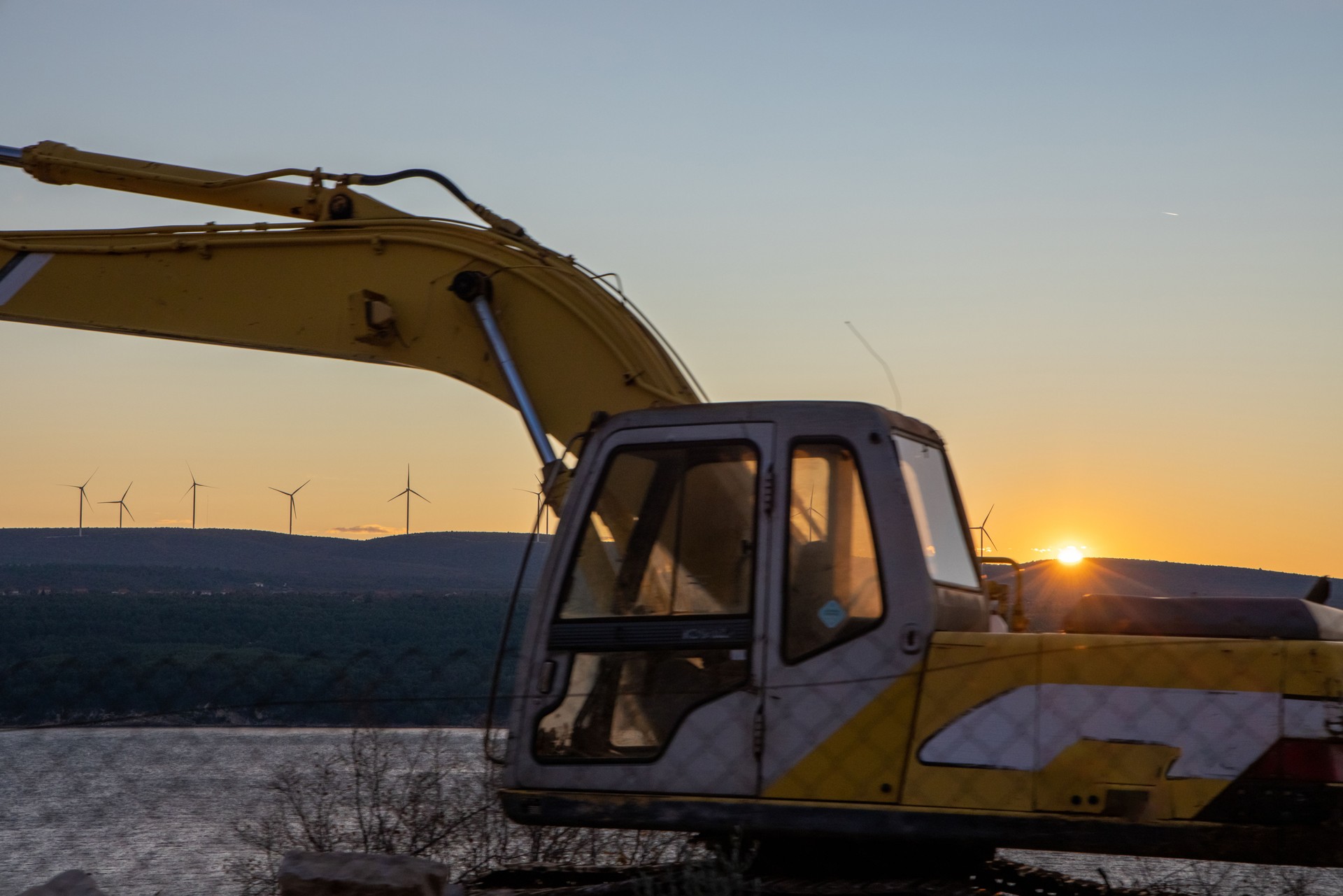 Excavator at Dusk with Wind Turbines in View
